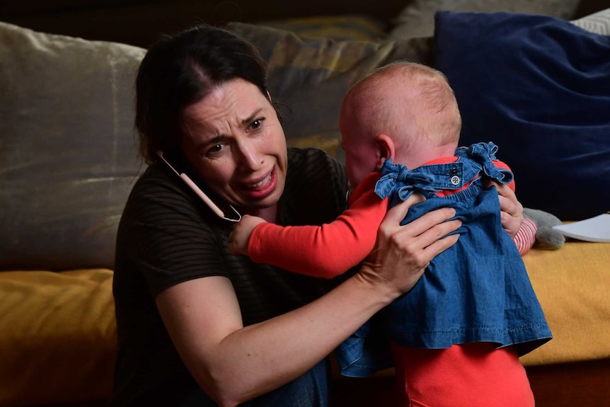 Alison Bell looks frantic as she holds a baby with a phone to her ear