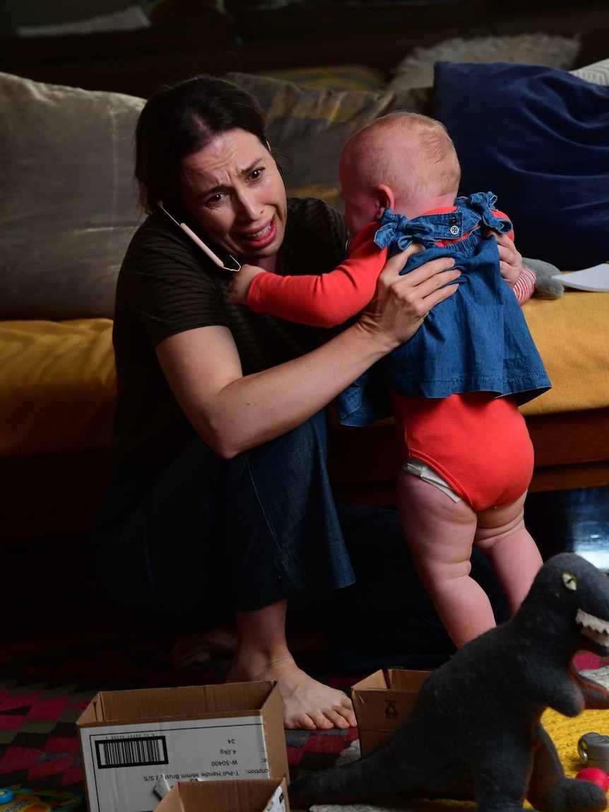 Alison Bell looks frantic as she holds a baby with a phone to her ear