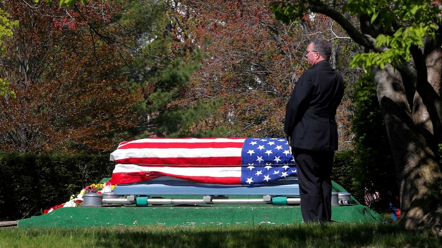 A US Marine stands beside the flag-draped coffin of a veteran who contracted the coronavirus disease.