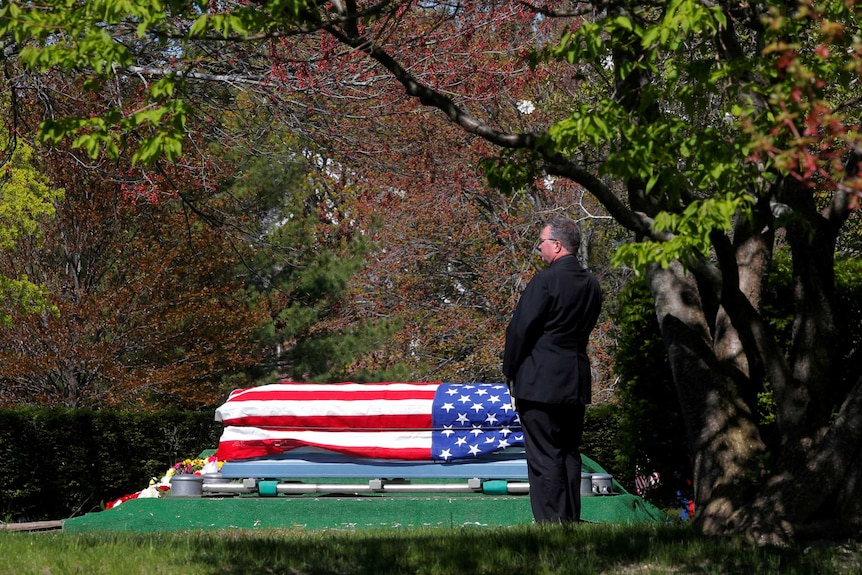 A US Marine stands beside the flag-draped coffin of a veteran who contracted the coronavirus disease.