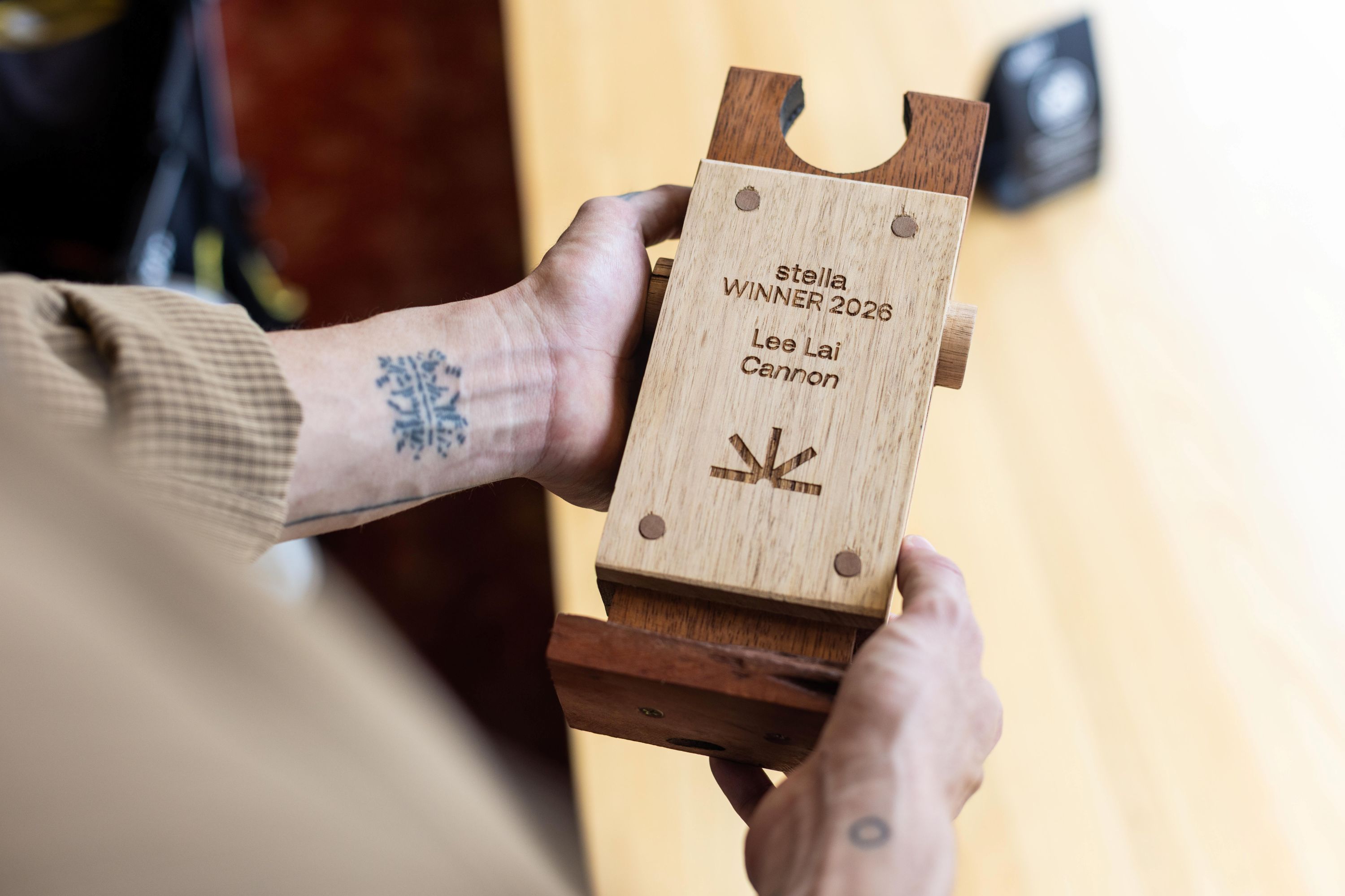 Las manos de una persona sostienen un trofeo de madera con la inscripción: 