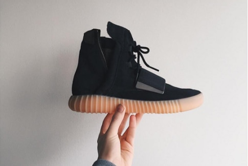 A hand holds a black pair of Adidas 'Yeezy' sneakers.
