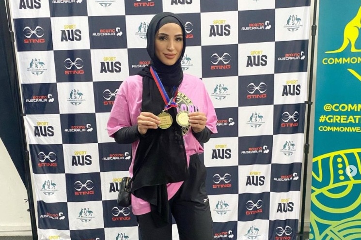 A hijab-wearing woman holds up two medals she won after winning a boxing contest