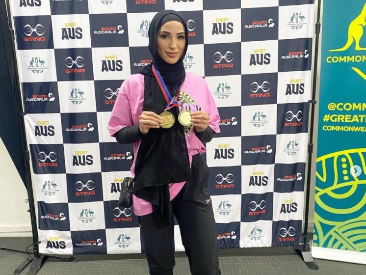 A woman in a hijab holds up two medals she won after winning a boxing competition
