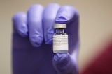 A gloved hand holds up a small vial of Pfizer's COVID-19 vaccine