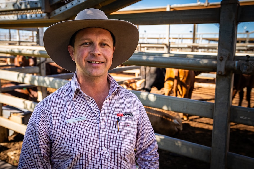 A man in a wide brimmed hat and shirt stands outside a cattle saleyard.