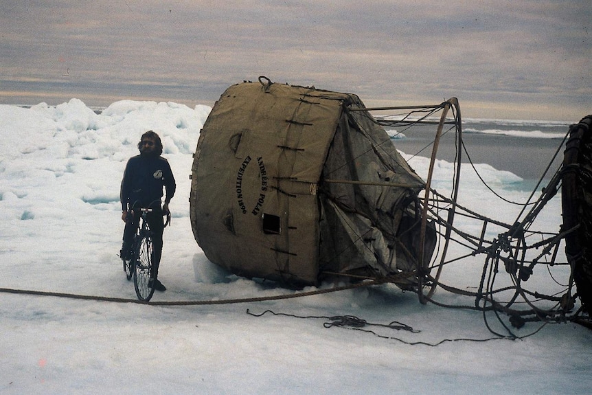 Cyclist with long hair and bushy beard on pack ice with hot air balloon basket on its side with "Andrees Polar Expedition 1896"