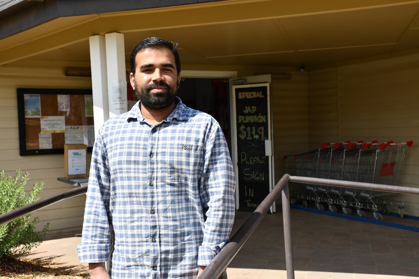 A man stands out the front of a building with some trolleys in the background