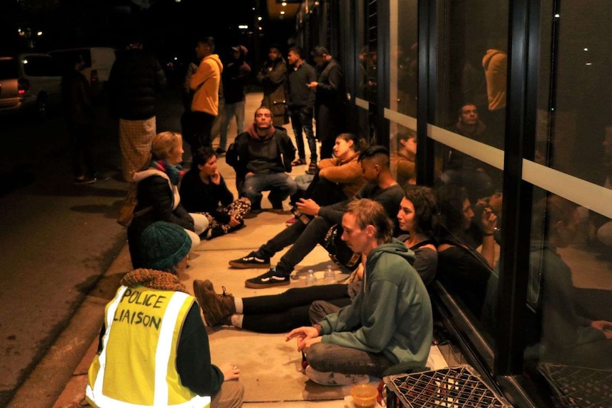 A group protestors sit on the floor at night outside a hotel