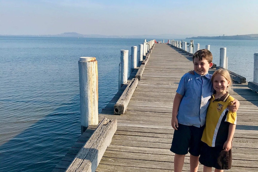two children stand on a pier surrounded by ocean