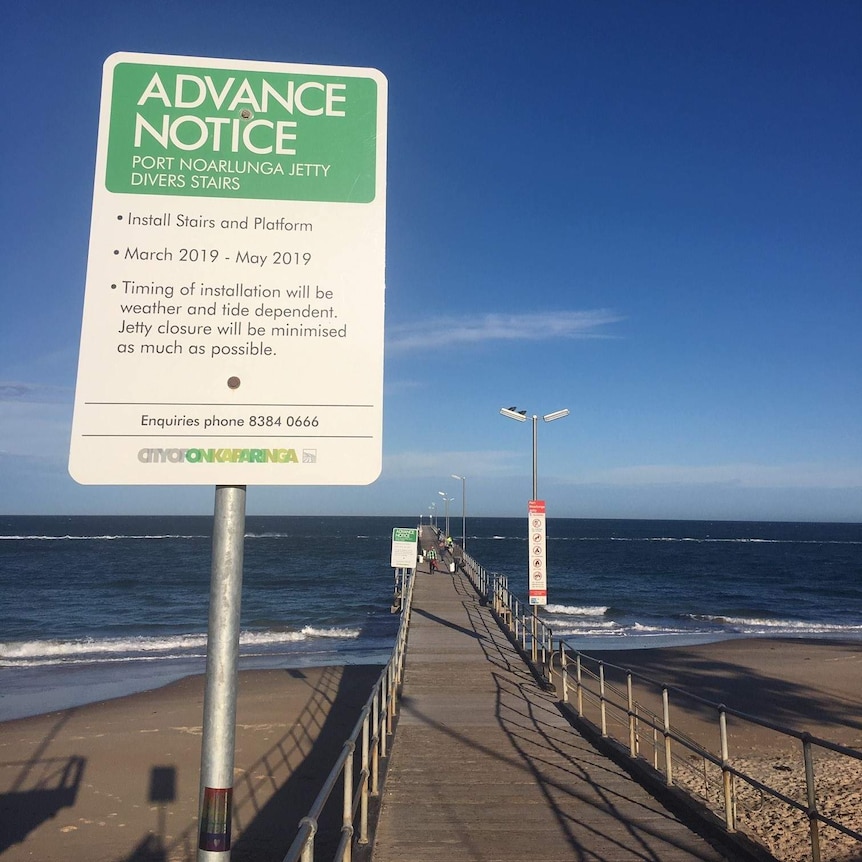 A sign at the start of a jetty with the sea behind