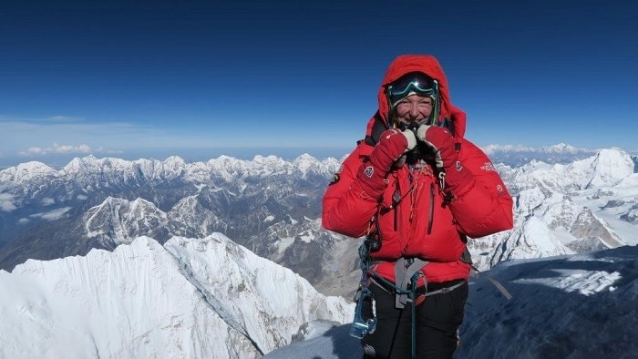 Woman in red jacket stands on mount Everest with snowy peaks below