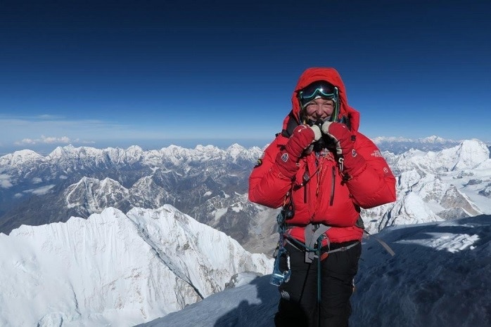 Woman in red jacket stands on mount Everest with snowy peaks below
