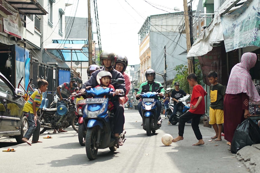 Scooters ride through soccer game in Tambora slum