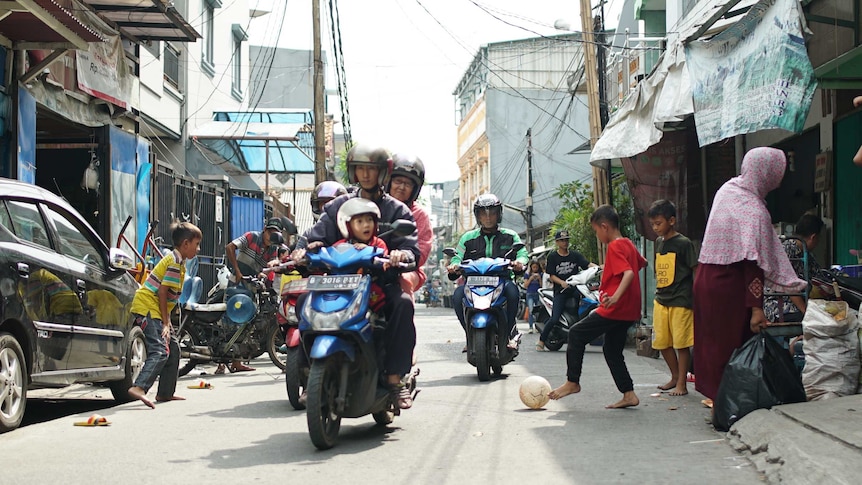 Scooters ride through soccer game in Tambora slum
