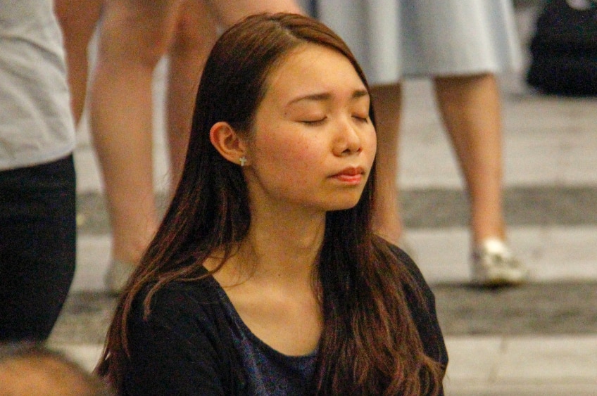 A young woman sitting on the floor with her eyes closed and a peaceful expression