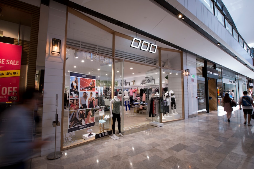 An activewear retail store with people walking past in a shopping centre.