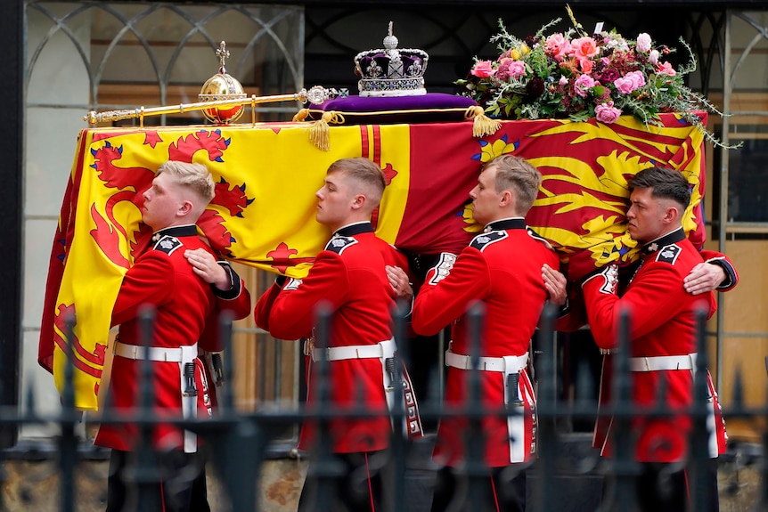 पालबियरर्स शाही मानक, लाल और पीले झंडे में लिपटे रानी के ताबूत को ले जाते हैं।