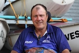 Townsville businessman Peter Gurr sits in his electric wheelchair inside a shed of sailing boats