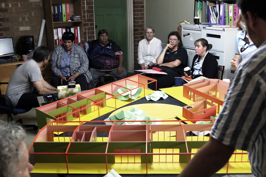 Several people sitting around a 3D model of the Murrin Bridge pre-school. 