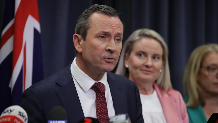 A close-up shot of WA Premier Mark McGowan speaking at a media conference indoors in front of a blonde woman.