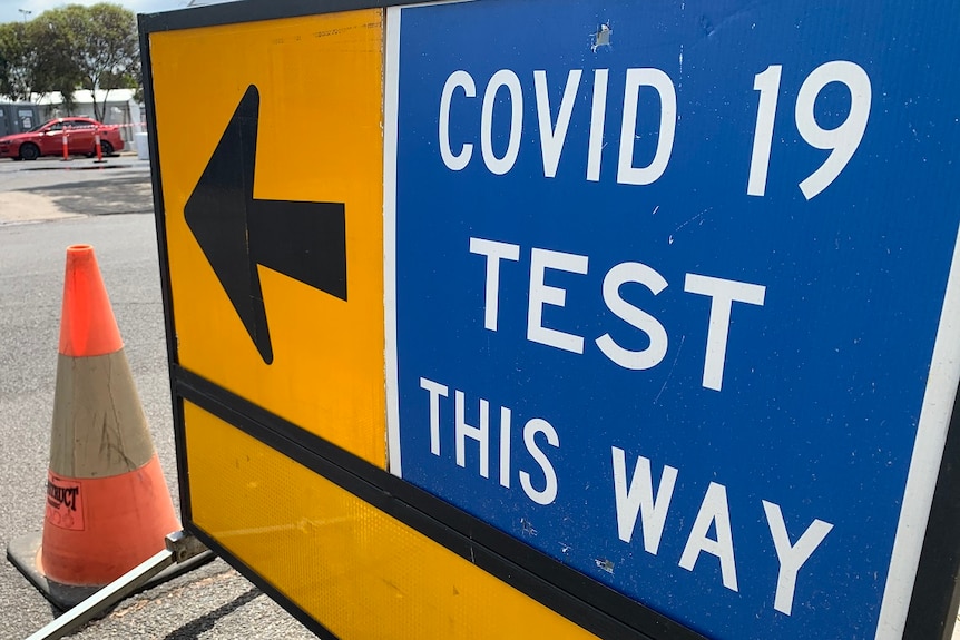 A blue sign reads "COVID-19 test this way", next to a yellow sick with a black directions arrow.