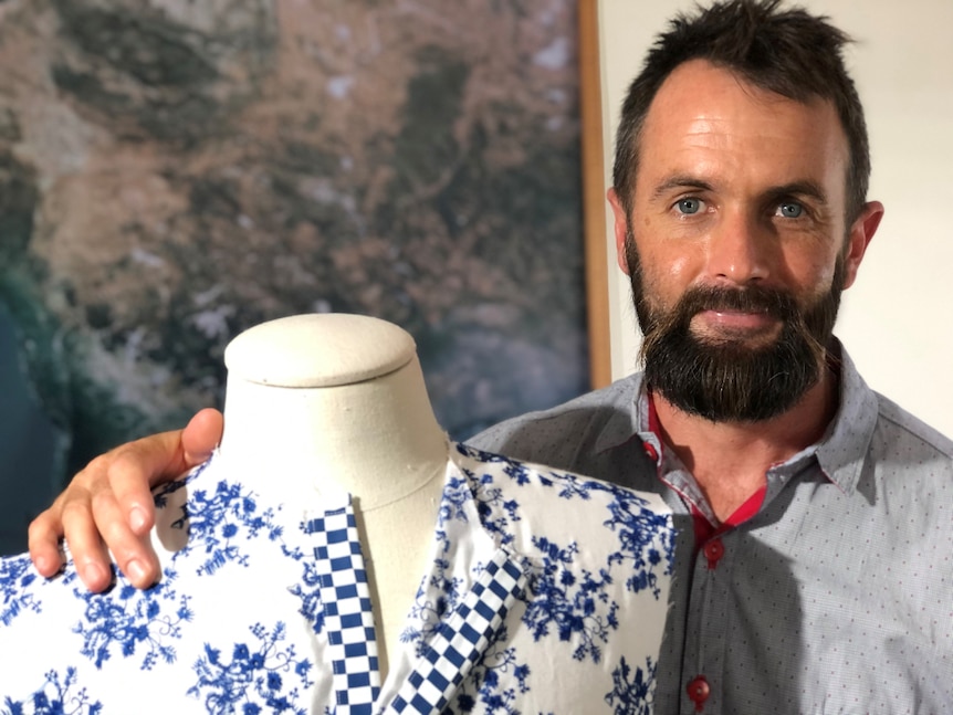 Man stands beside dress mannequin which has fabric with blue and white flowers and blue and white checks