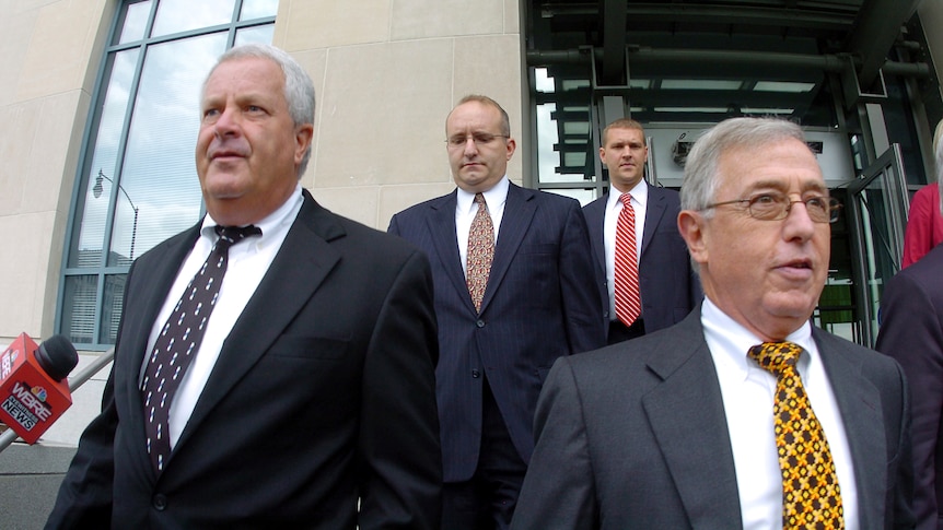 Two former judges in suits, lawyers behind them, on the courthouse steps