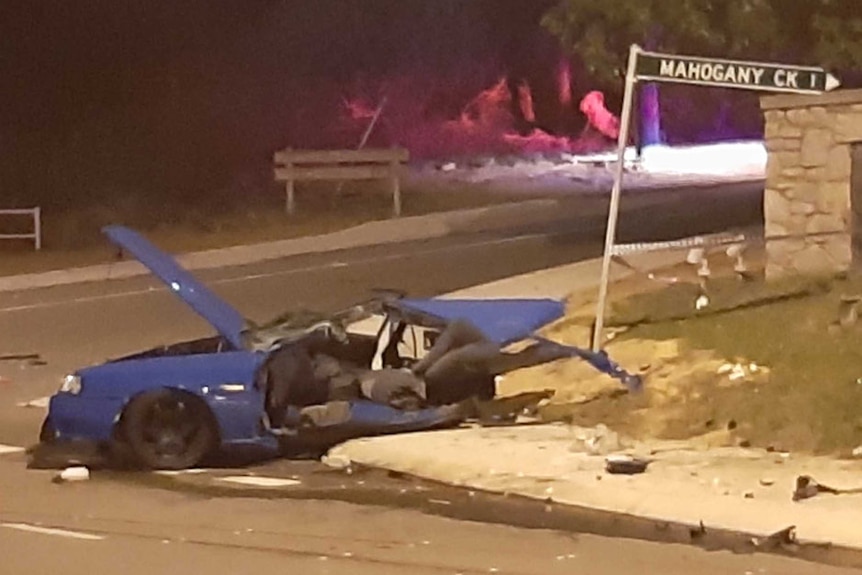 A badly damaged car, with parts strewn all around it.