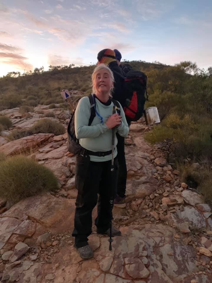 Woman wearing a peppermint green top and black pants. Carrying a pack walking on a hiking track.