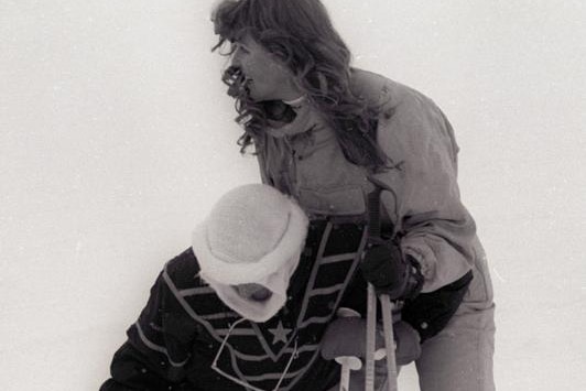 Princess Diana, left, wears a dark ski suit as she half-stands on her skiis while held up by Sarah Ferguson, in light ski suit.