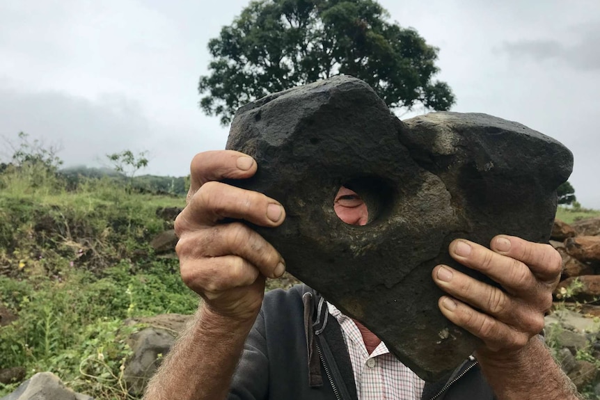 Ian Elliott holding up a heart shaped rock with a hole in it.