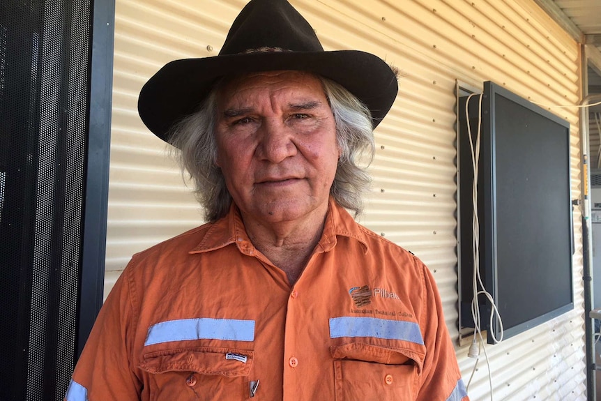 A mid-shot of Banjima man Marshall Smith wearing a hi-vis shirt and a wide-brim hat standing in front of a house.