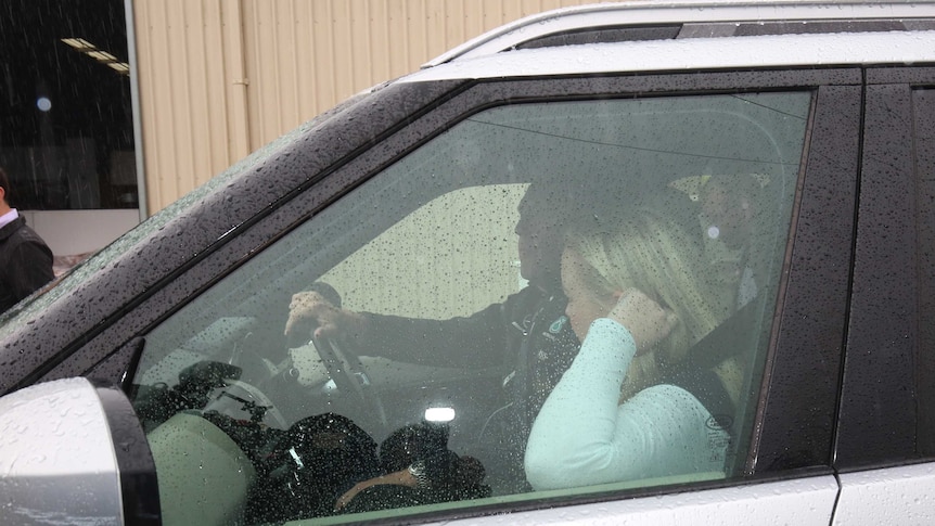 Jessica Whelan holds her hand to her head as she sits in a car covered in rain