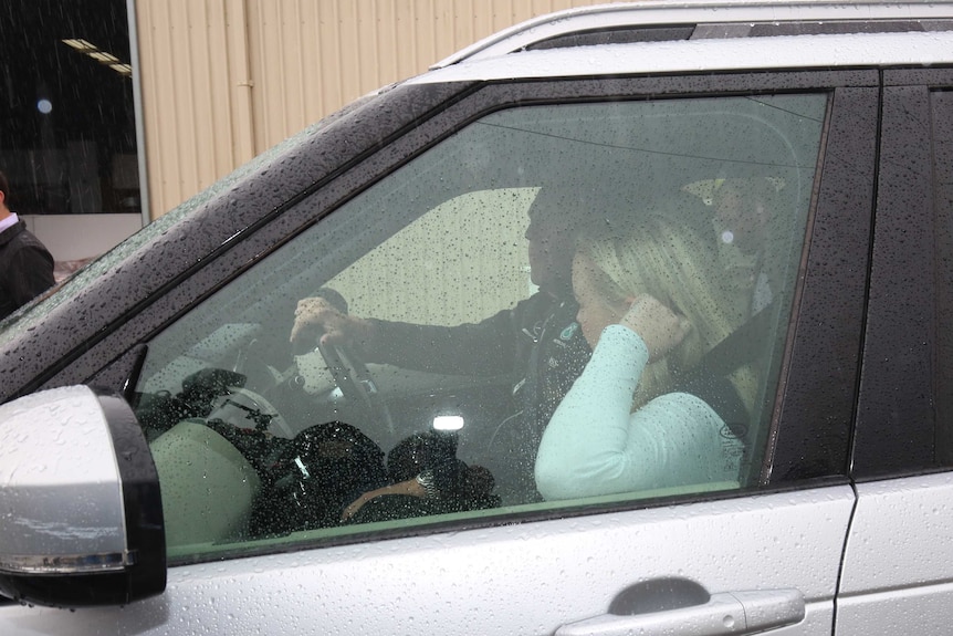 Jessica Whelan holds her hand to her head as she sits in a car covered in rain