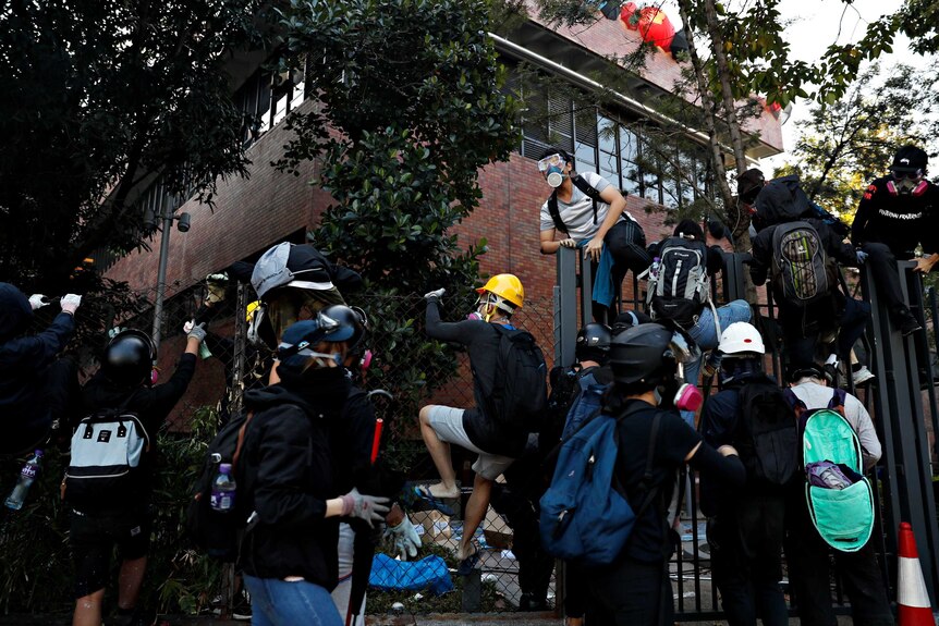 Several protesters jumping a fence inside a Hong Kong university trying to escape police