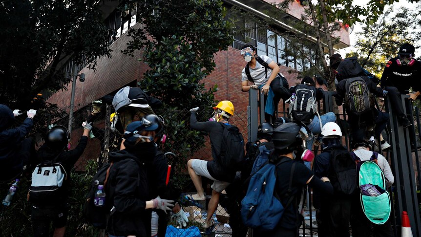 Several protesters jumping a fence inside a Hong Kong university trying to escape police