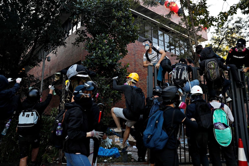 Several protesters jumping a fence inside a Hong Kong university trying to escape police