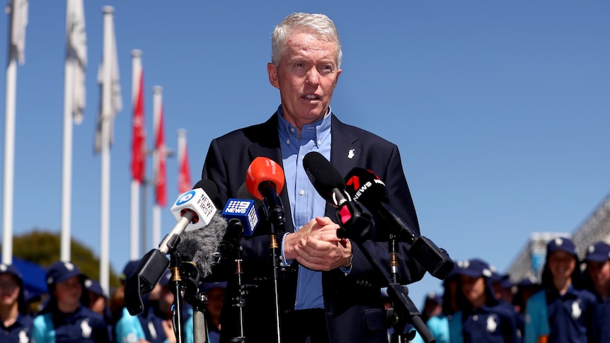 Australian Open tournament director Craig Tiley stands in front of microphones, with a row of flags in the background .