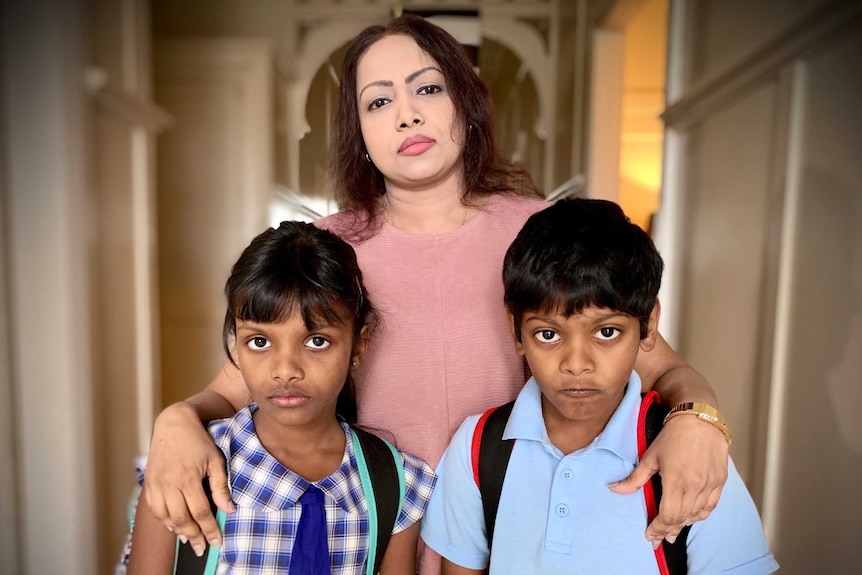 A woman and her two children look to the camera with concerned expressions.