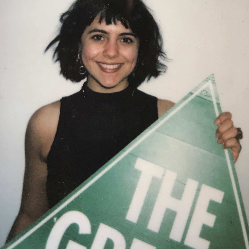 Woman holds a triangle sign saying "The Greens".