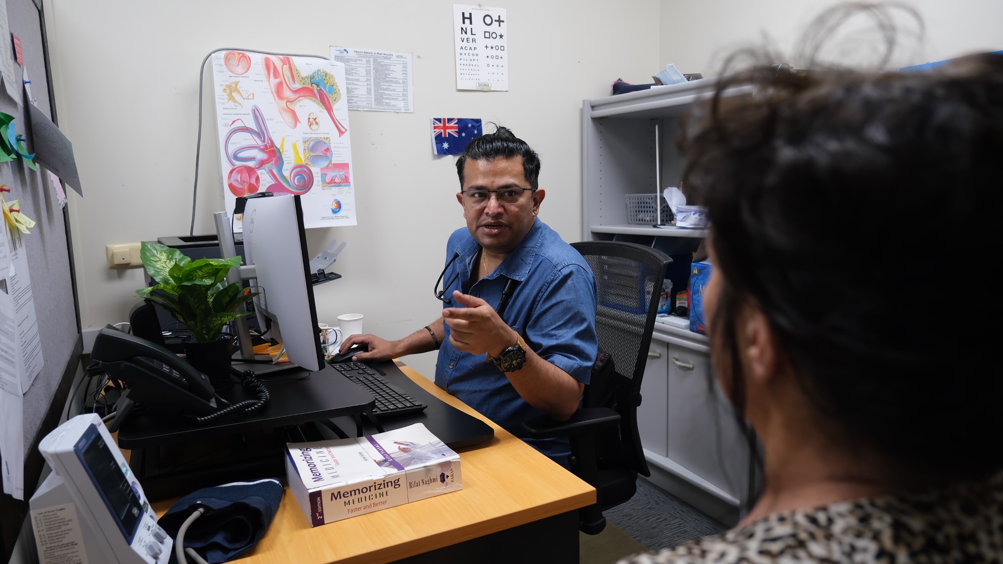 Um médico sentado em frente ao computador conversa com um paciente não identificado.