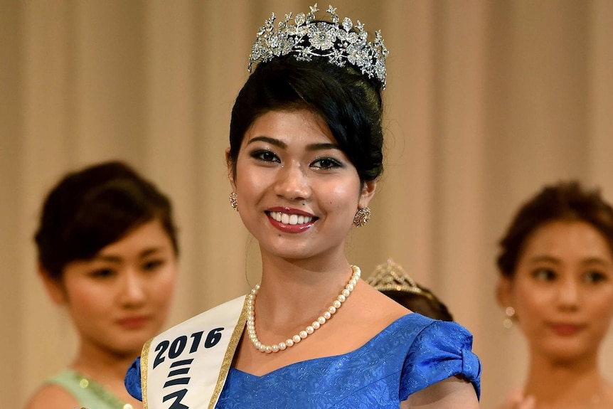 Priyanka Yoshikawa smiles wearing a Miss Japan sash and holding a trophy