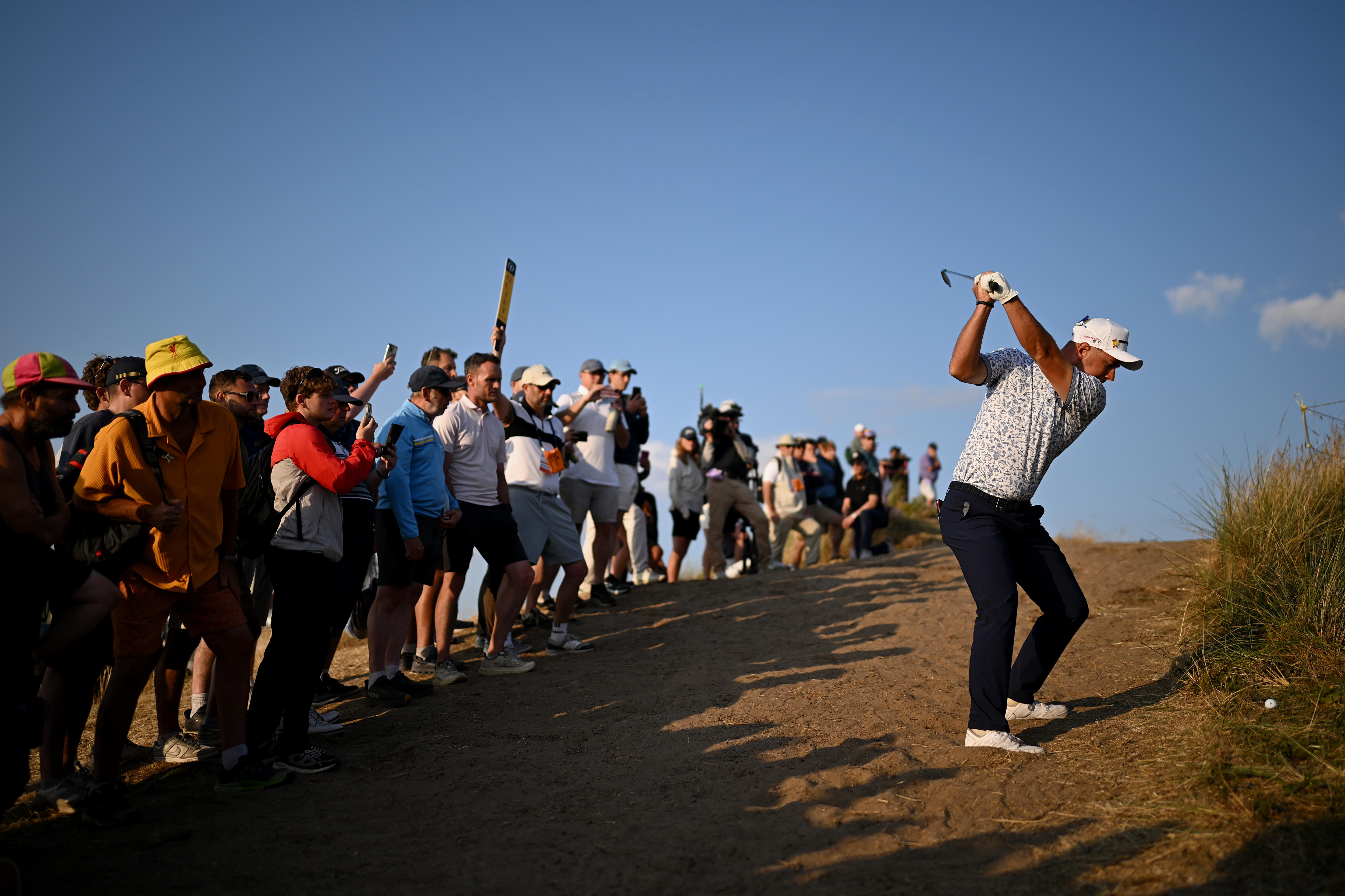 A golfer plays a difficult shot out of sand.