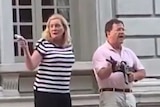 A woman in a striped t-shirt and a man in a pink shirt holding guns as they stand on their front lawn.
