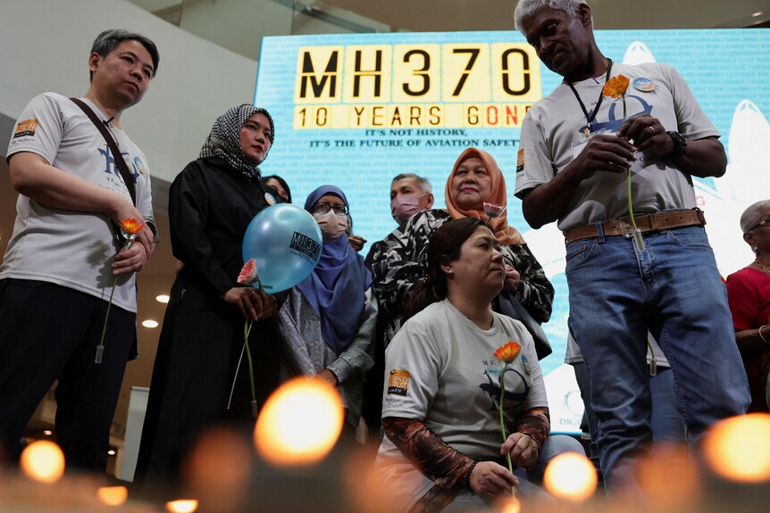 A group of people stand in front of a sign that reads "MH370, 10 years on".