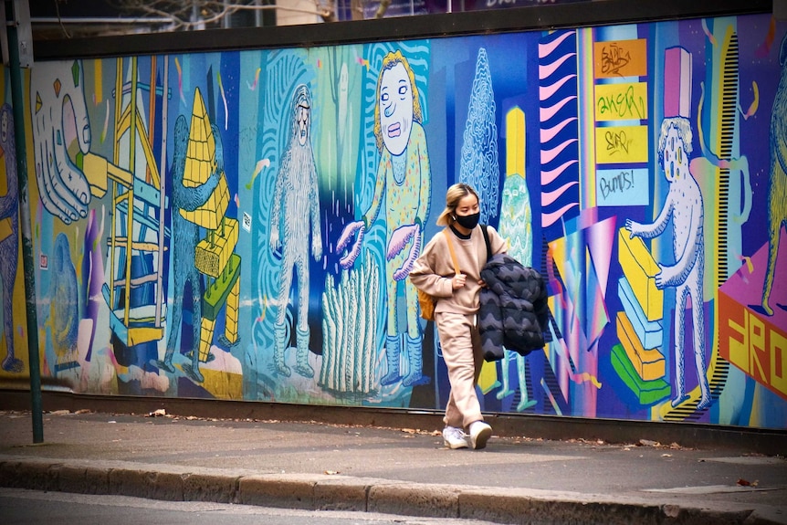 A masked pedestrian walks along a deserted Sydney street in lockdown.