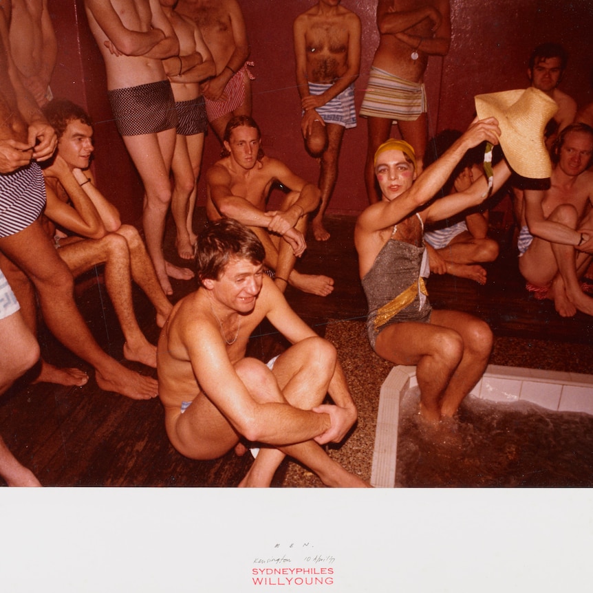 Men in bathers sit around a sauna together laughing