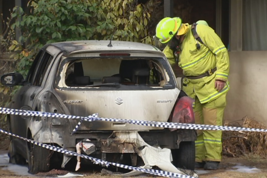 A firefighter inspects the shell of a burnt out car in front of a home in Canberra.