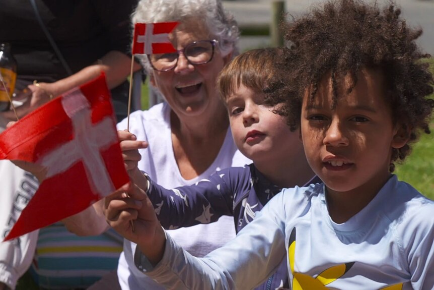Two young kids and an elderly woman wave miniature Danish flags. 